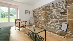 Quarto com parede de pedra, mesa de vidro, cadeira de madeira e uma cama.