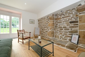 Una habitación con pared de piedra, una mesa de vidrio, una silla de madera y una cama.