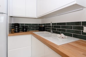 Una cocina moderna con armarios blancos, encimera de madera, un lavabo y una cafetera.