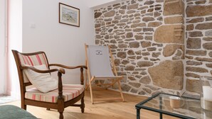 Quarto com cadeira de madeira, quadro branco, mesa de vidro e parede de pedra.