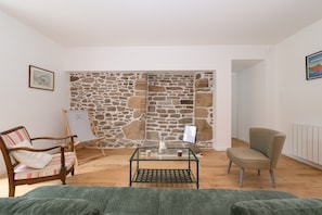 Una habitación con pared de piedra, una silla de madera, una mesa de vidrio y un sofá verde.