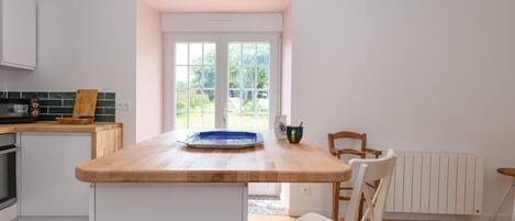 A kitchen with a wooden countertop, white cabinets, a window, and a view of greenery outside.