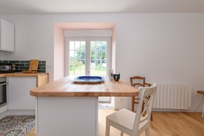 Una cocina con encimera de madera, armarios blancos, un ventanal y vistas al verdor exterior.