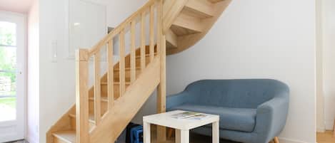 Un interior moderno con una escalera de madera, un sofá azul y una pequeña mesa blanca.