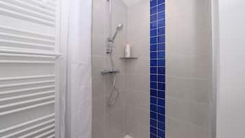 Eine Dusche mit Duschbrause und Wandarmatur, ein weißer Handtuchhalter und eine kleine Ablage mit einer Flasche.