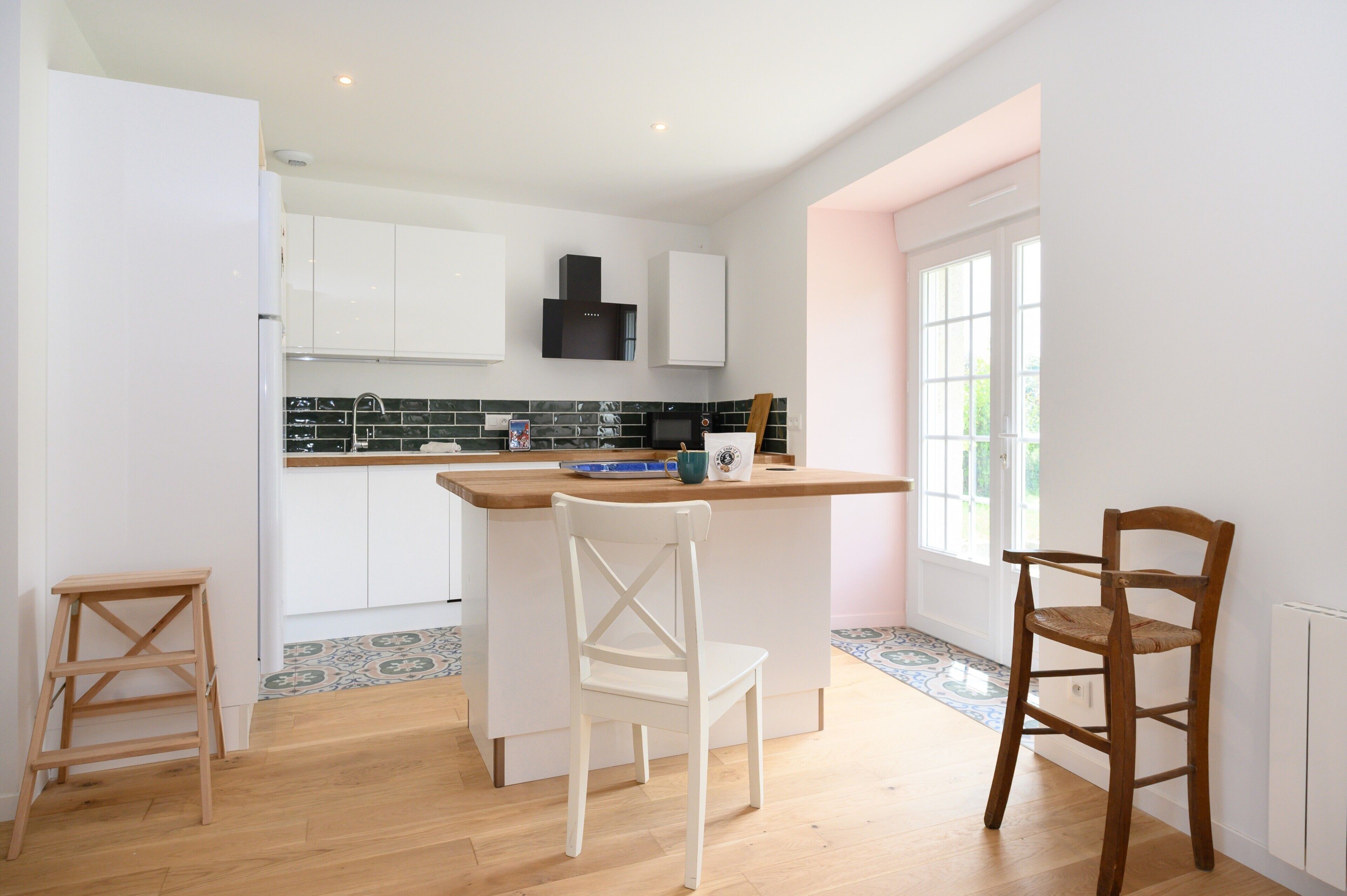 Una cocina con gabinetes blancos, una campana extractora negra, encimera de madera y salpicadero de azulejos.