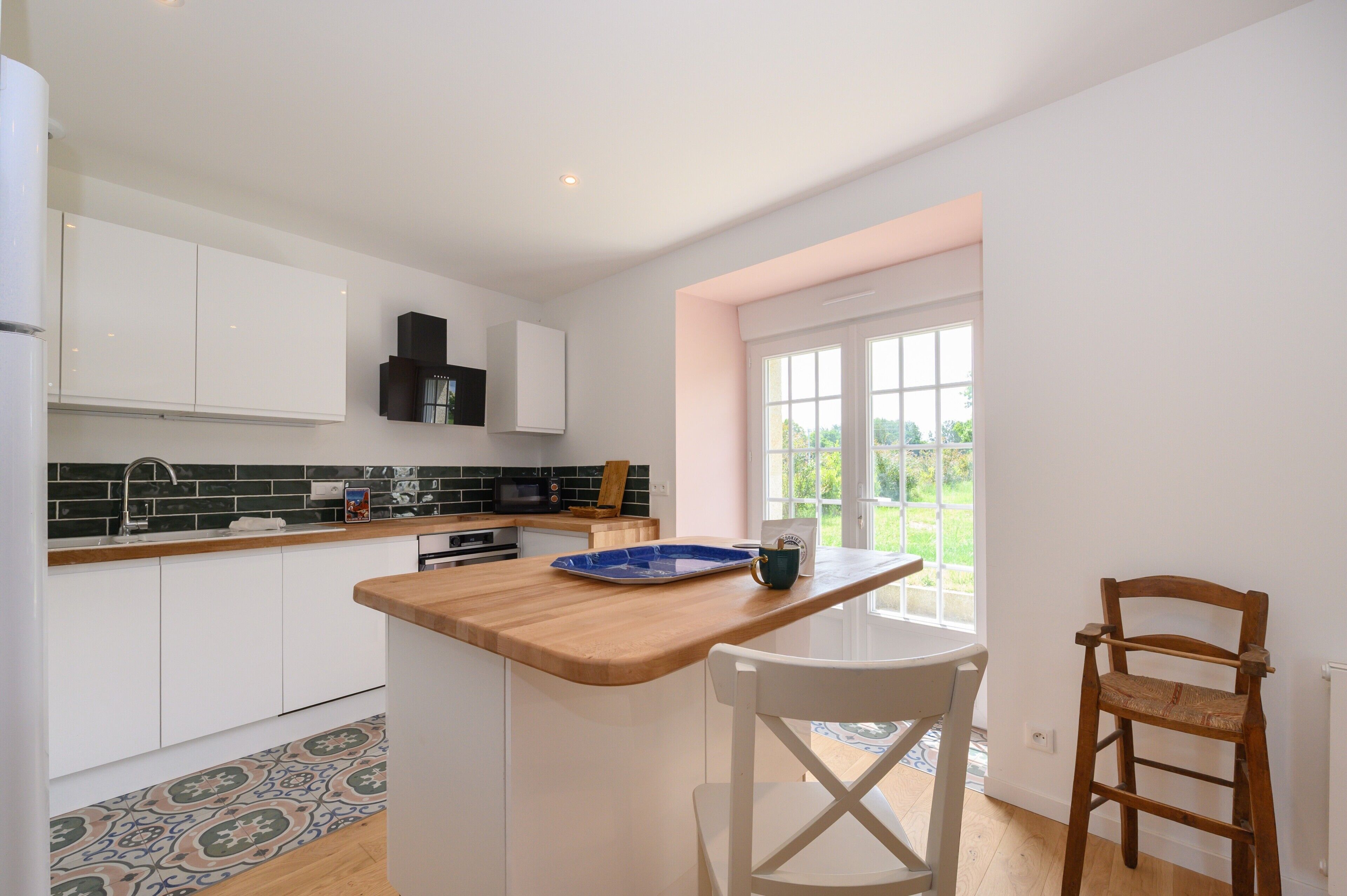 A modern kitchen with white cabinets, a wooden countertop, and a window with a view of greenery.