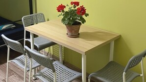 Ett litet matområde med ett träbord och fyra stolar med hålmönster. En krukväxt med röda blommor står på bordet.