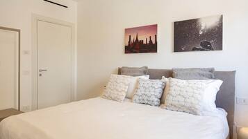Una camera da letto con un letto, cuscini, un comodino e due opere d'arte appese al muro.
