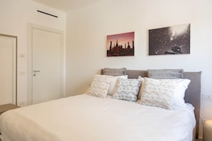 Ein Schlafzimmer mit einem Bett, Kissen, einem Nachttisch und zwei an der Wand befestigten Kunstwerken.