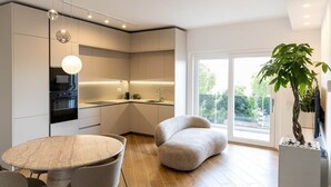 A modern kitchen with built-in appliances, a dining area with a round table, and a large window with a view of greenery. - DKV Collection 15-Elegant Apt 2BedRooms Pigneto MetroC (Rome)