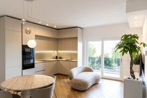 Eine moderne Küche mit Einbaugeräten, ein Essbereich mit einem runden Tisch und ein großes Fenster mit Blick auf Grünflächen.
