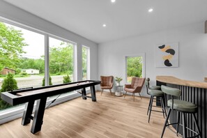 Ein modernes Zimmer mit Billardtisch, Barbereich und großen Fenstern.