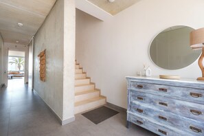 A staircase leading to another level, a wooden dresser with drawers, a round mirror, and a wall-mounted lamp. - Villa Lumina w/ Arcade & Pool, PS5 (Can Picafort)