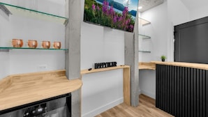 A modern kitchen with a wooden countertop, a black refrigerator, and a glass shelf with copper mugs.