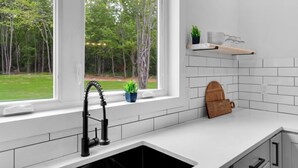 A kitchen with a window, a sink, a shelf with kitchenware, and a plant.