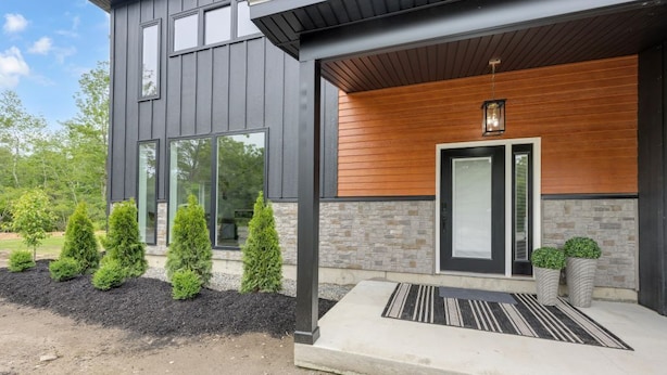 A modern two-story house with a dark exterior, large windows, a wooden accent wall, and a well-maintained front yard with trimmed bushes.