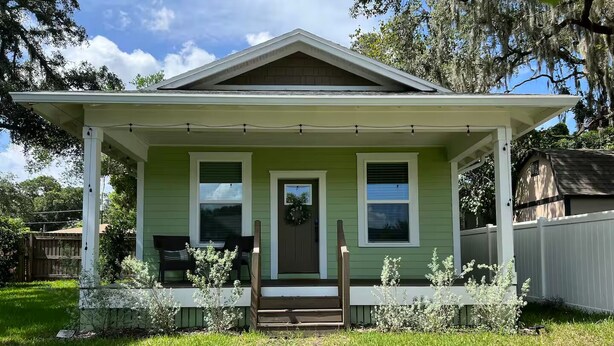 Una casa verde con veranda, porta d'ingresso e un piccolo giardino.