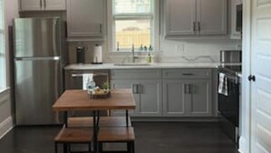 Una cucina con mobili grigi, un frigorifero in acciaio inossidabile, un tavolo di legno con panche e una finestra.