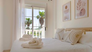 A hotel room with a bed, towels, a wooden headboard, and two wall art pieces. - Marena Resort Townhouse (Oliva)