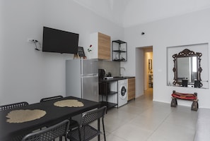 Eine moderne Küche mit Kühlschrank, Mikrowelle und Spüle. Ein Esstisch mit Stühlen und einer Bank lädt zum Verweilen ein. Ein Fernseher ist an der Wand befestigt.