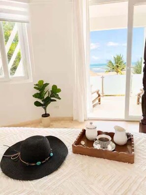 A room with a view of the beach, a potted plant, a tray with a teapot and cups, and a black hat on a white rug. - Beachfront Estate | Pool, Theater, Sleeps up to 24 (Sabaneta de Yasica)