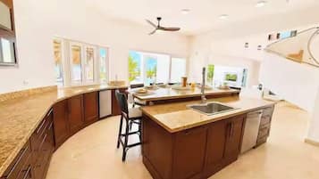 A modern kitchen with a curved island, bar stools, and a large window providing natural light.