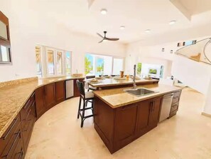 A modern kitchen with a curved island, bar stools, and a large window providing natural light. - Beachfront Estate | Pool, Theater, Sleeps up to 24 (Sabaneta de Yasica)