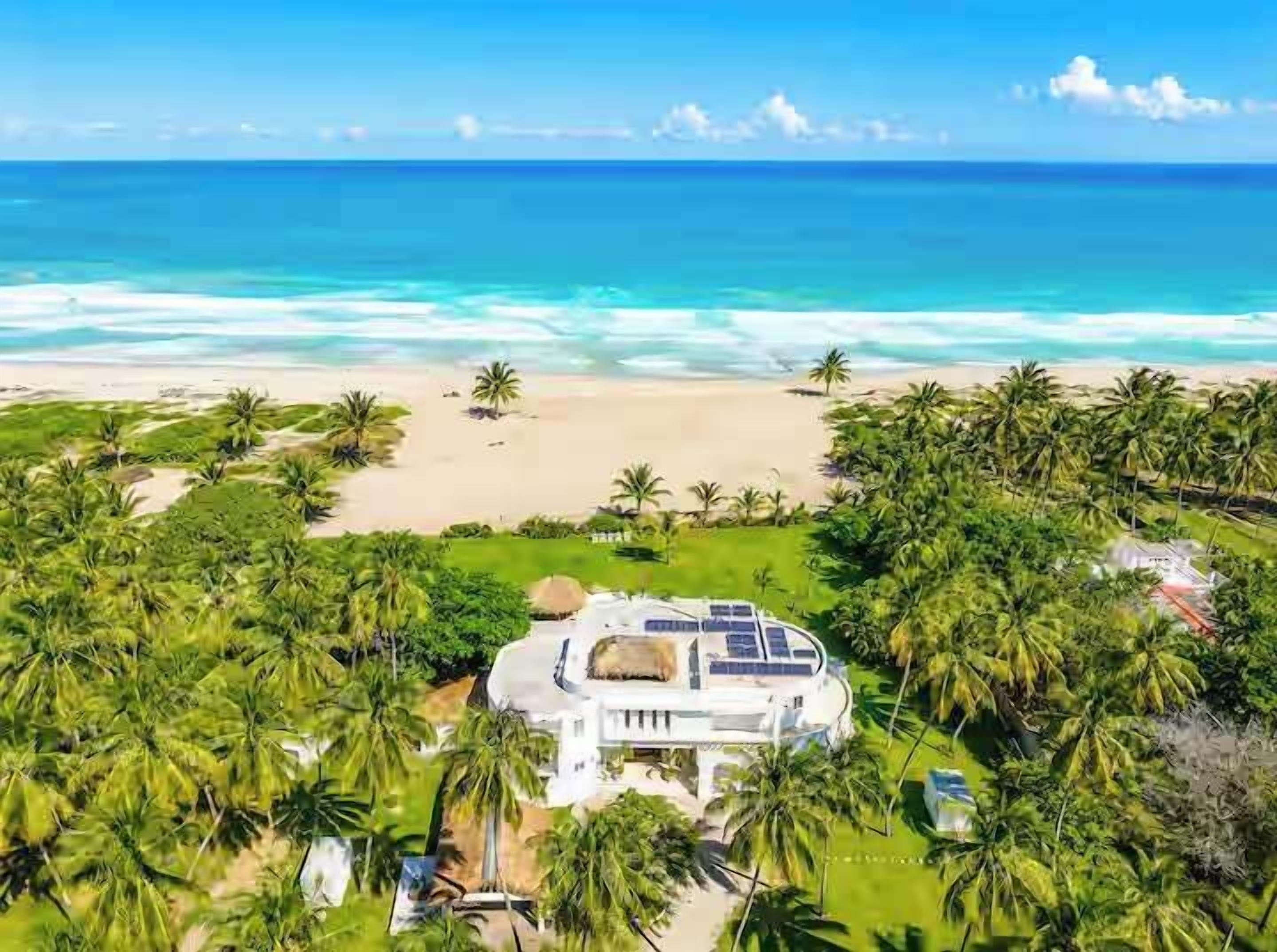 A beachfront property with a large house, solar panels, and lush greenery.