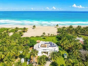 A beachfront property with a large house, solar panels, and lush greenery. - Beachfront Estate | Pool, Theater, Sleeps up to 24 (Sabaneta de Yasica)