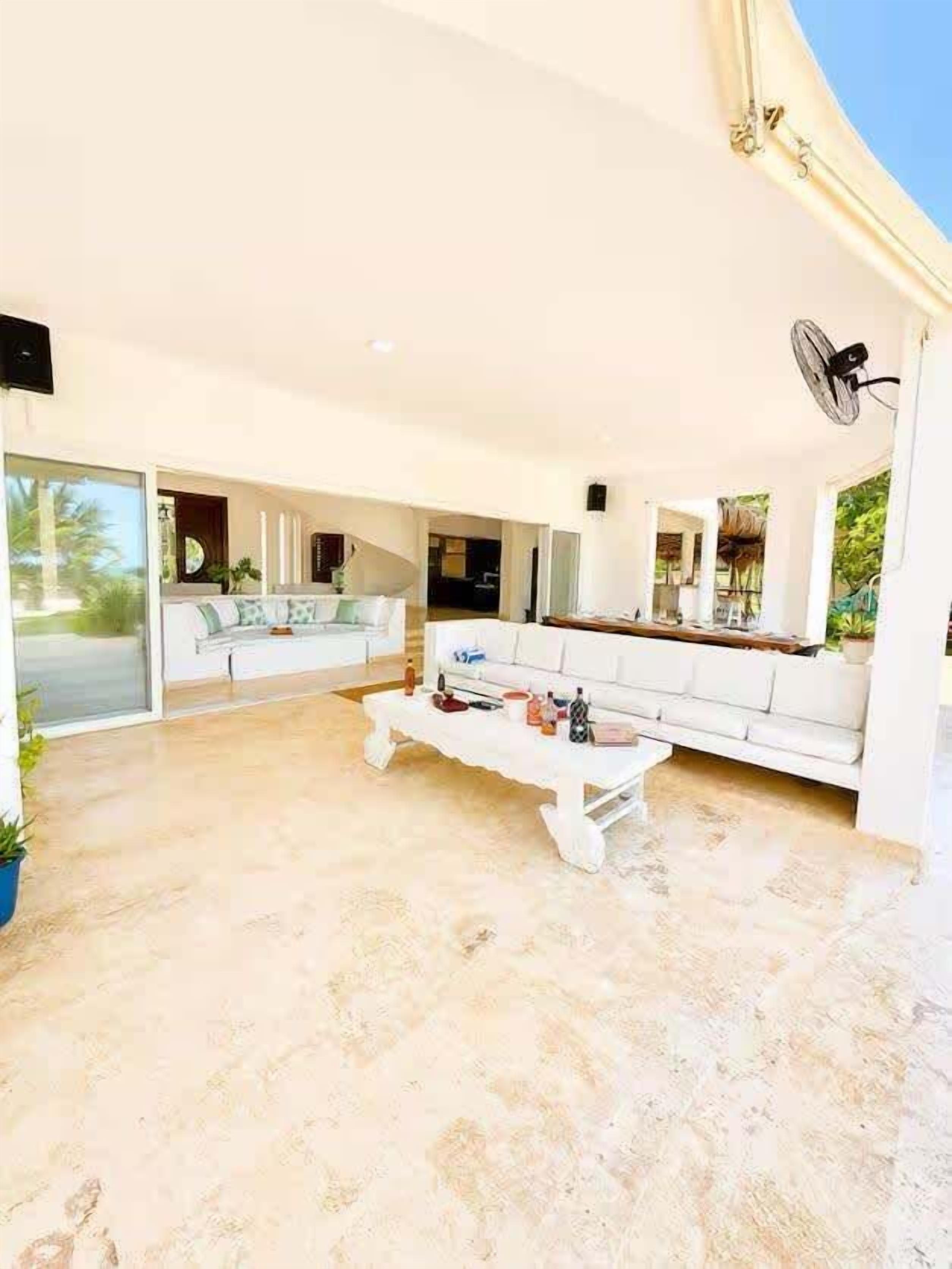 A spacious living area with a white sofa, a coffee table, and a fan.
