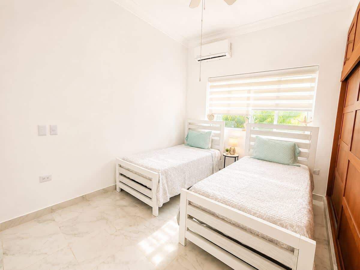 A bedroom with two beds, a window with blinds, an air conditioning unit, and a marble floor.