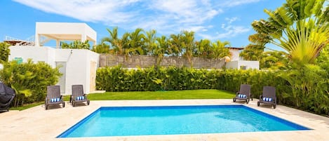 Ein Swimmingpool mit Liegestühlen, umgeben von Grünpflanzen und blauem Himmel.