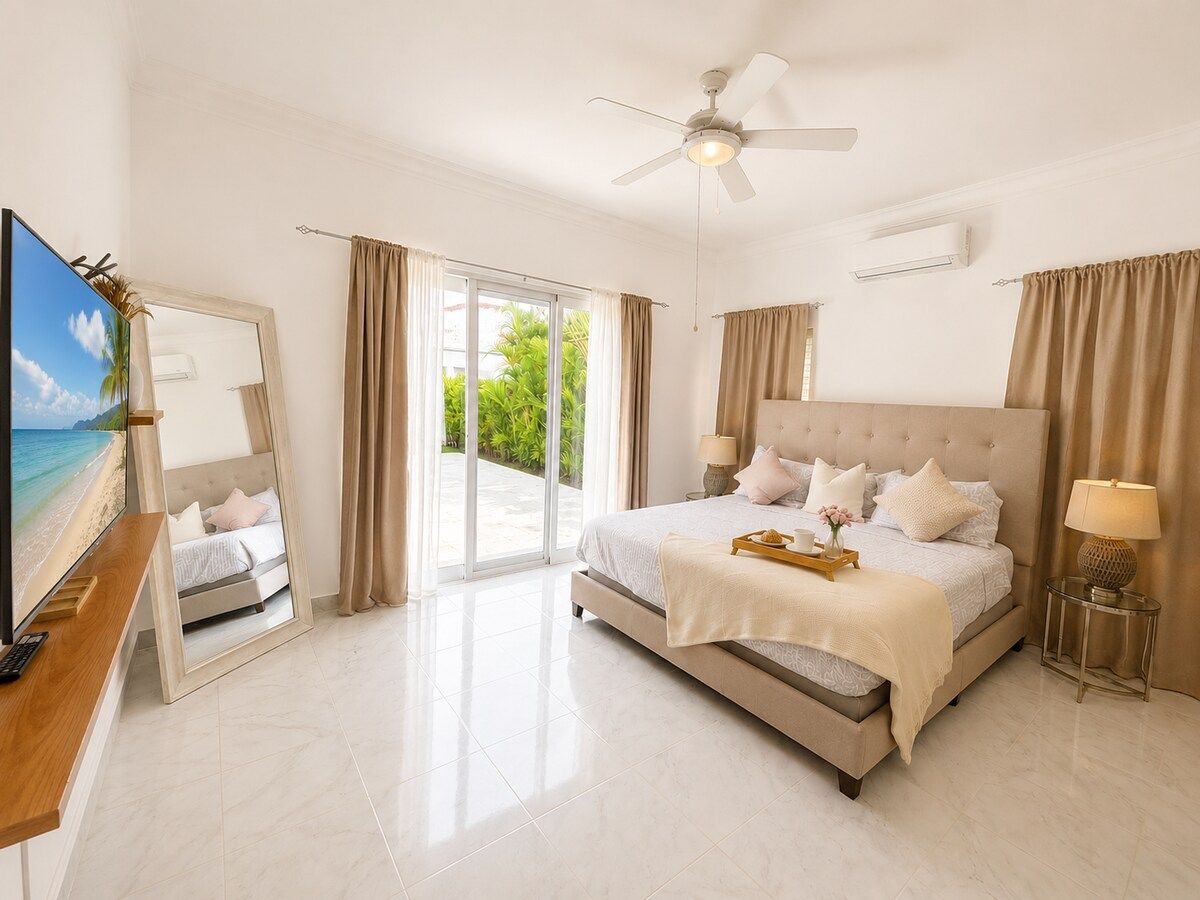 A spacious bedroom with a large bed, a ceiling fan, and a view through the glass door.