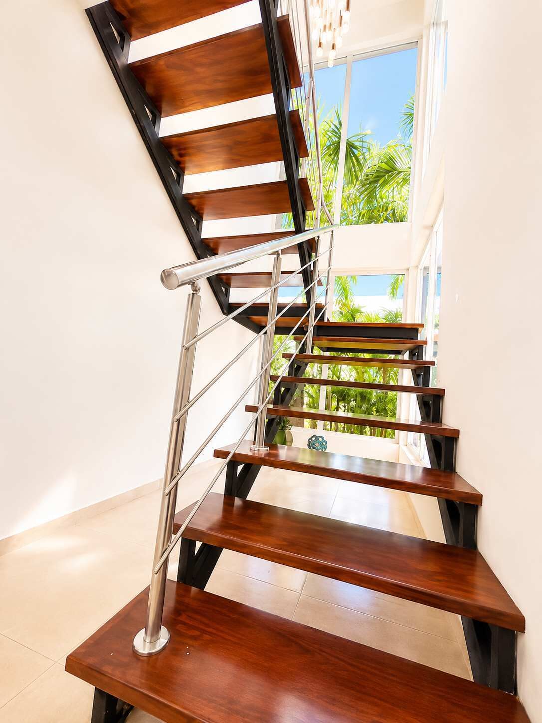 A modern staircase with wooden steps and metal railings, leading to a balcony with a view of greenery.