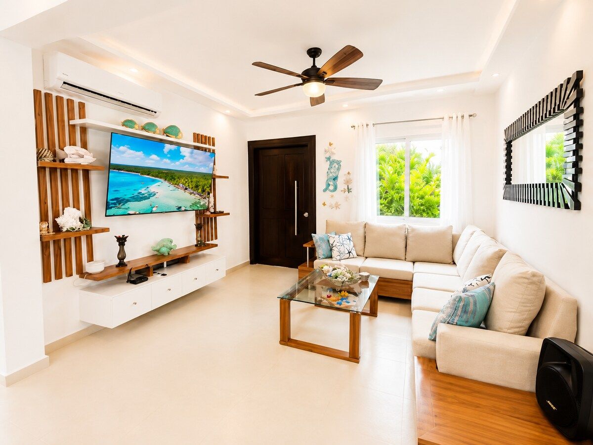A modern living room with a flat-screen TV, a ceiling fan, a sofa, and a coffee table.