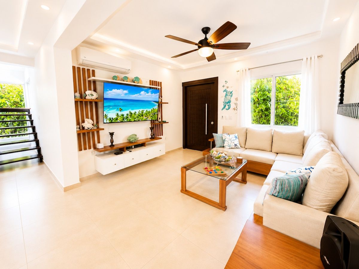 A modern living room with a flat-screen TV, a ceiling fan, a sofa, and a coffee table.