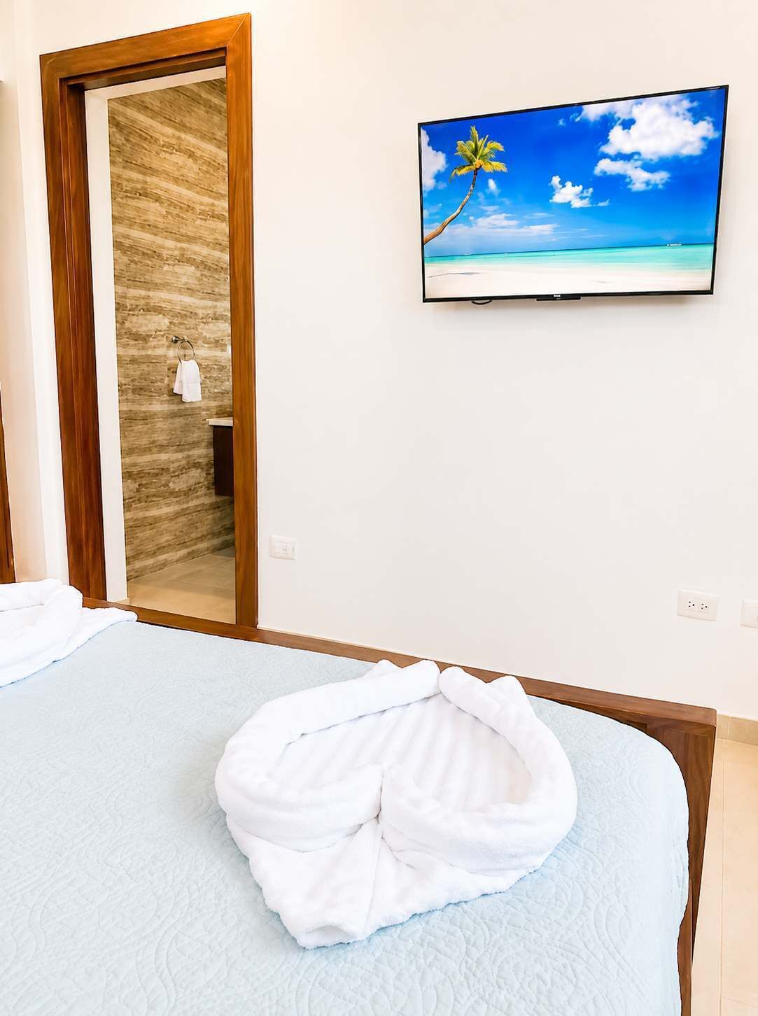 A hotel room with a bed, a television on the wall, and a door leading to a bathroom.
