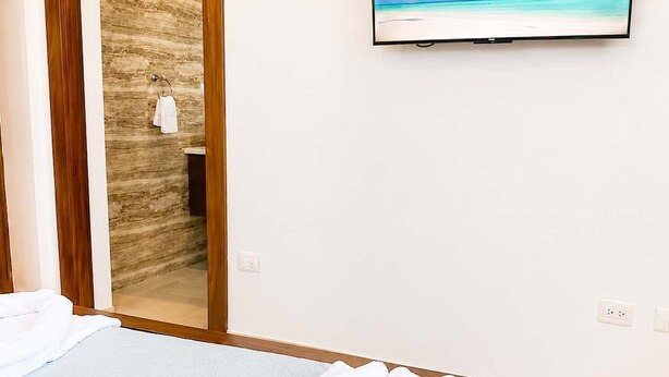A hotel room with a bed, a television on the wall, and a door leading to a bathroom. - 3 Suites | L-Shaped Pool & Caribbean Retreat (Sosúa)