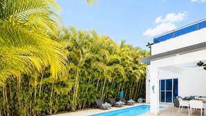 A swimming pool with a tiled deck, surrounded by palm trees and a modern building with a balcony. - 3 Suites | L-Shaped Pool & Caribbean Retreat (Sosúa)