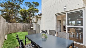 A patio with a table and chairs, a wooden fence, and a building with a white exterior. - Mariners in the Village (Shellharbour)