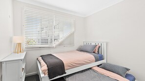 A bedroom with a bed, bedside table, and window blinds. - Mariners in the Village (Shellharbour)