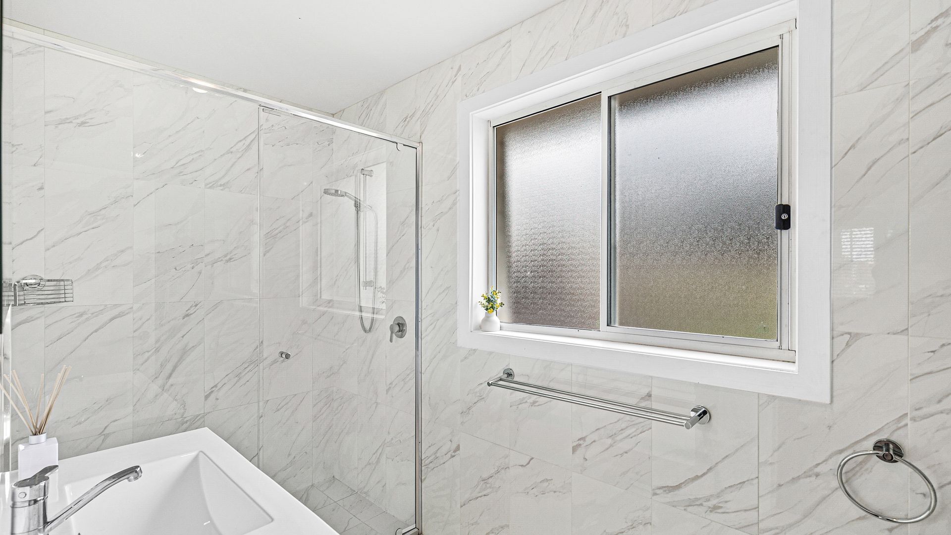 Un baño con ducha, lavamanos y ventana con vidrio esmerilado.