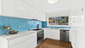 Una cucina moderna con mobili bianchi, schienale blu, piano cottura a gas, forno e lavastoviglie.