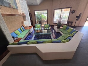A modern living room with a sectional sofa, a glass coffee table, and a bookshelf. - Unique Seaside Retreat - with Chef & Staff (Chicxulub, Yucatan, Mexico)