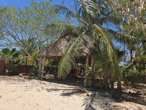 A thatched-roof hut with a sandy ground and palm trees. - Unique Seaside Retreat - with Chef & Staff (Chicxulub, Yucatan, Mexico)
