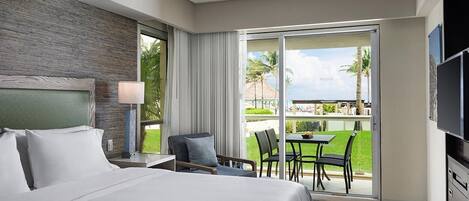 Una habitación de hotel con una cama grande, un escritorio, una silla, un televisor y un balcón con vistas a palmeras y un edificio.