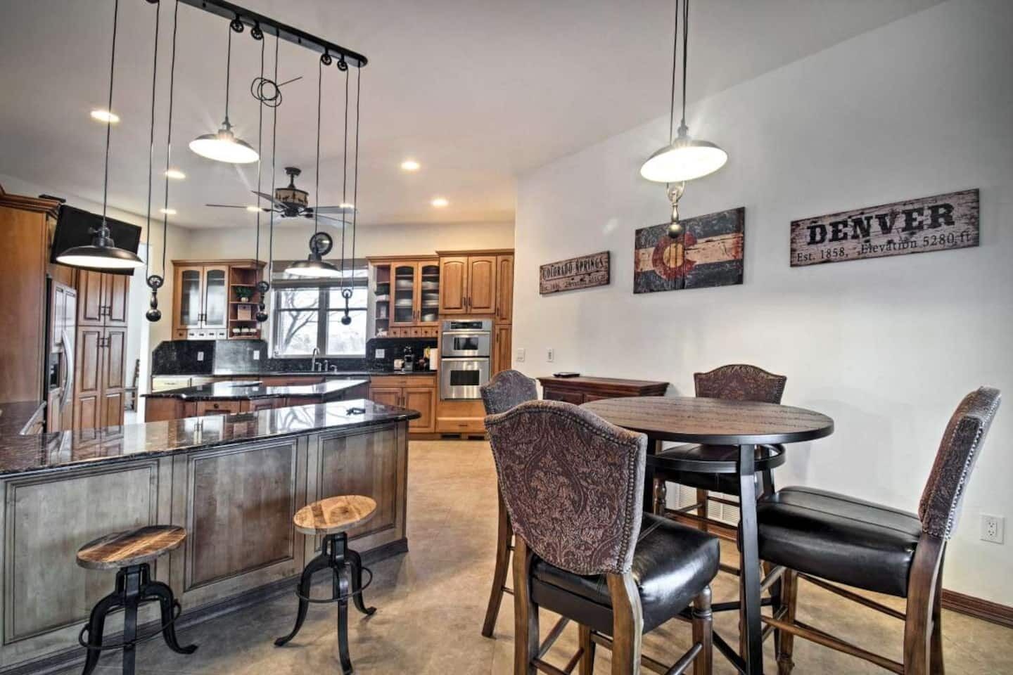 A modern kitchen with a central island, dining area with a round table and chairs, and a ceiling fan.