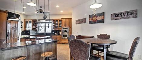 A modern kitchen with a central island, dining area with a round table and chairs, and a ceiling fan.