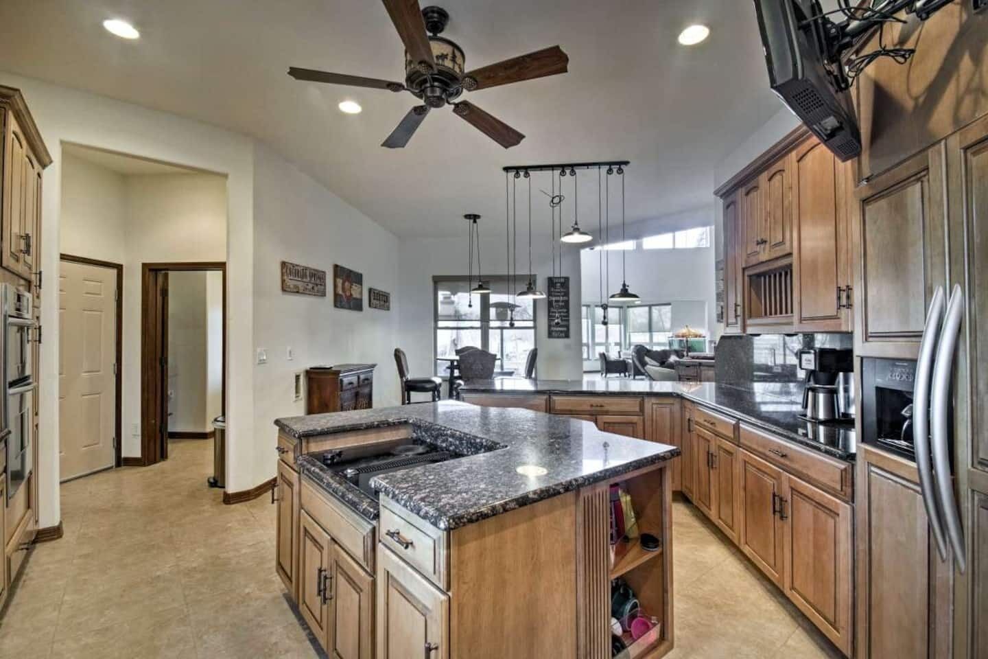 A spacious kitchen with wooden cabinets, a granite countertop island, a ceiling fan, and a large window providing natural light.